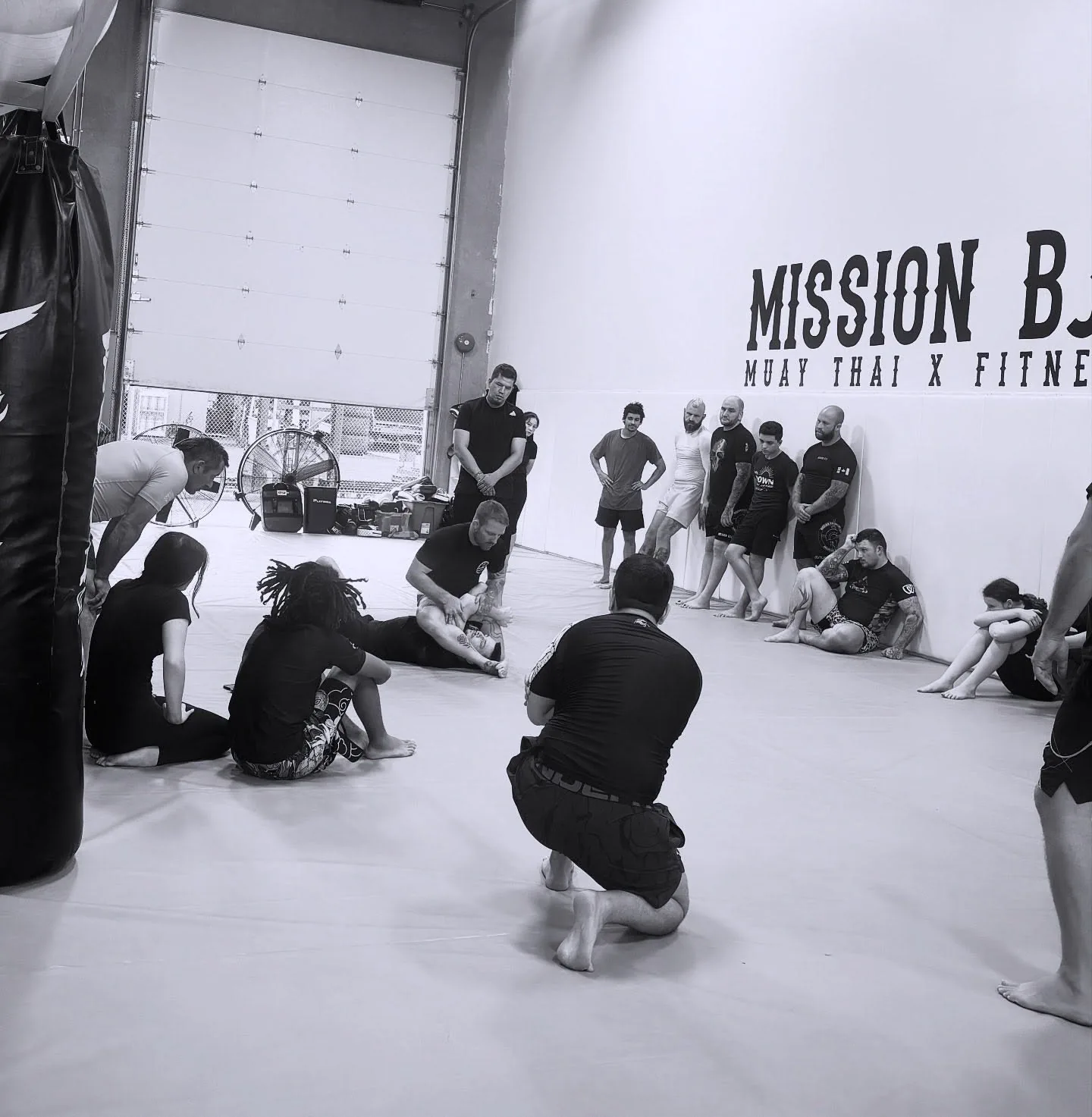 Coach leading a Brazilian Jiu Jitsu class on the mats in front of the painted Mission BJJ wall at the academy in Mission, BC