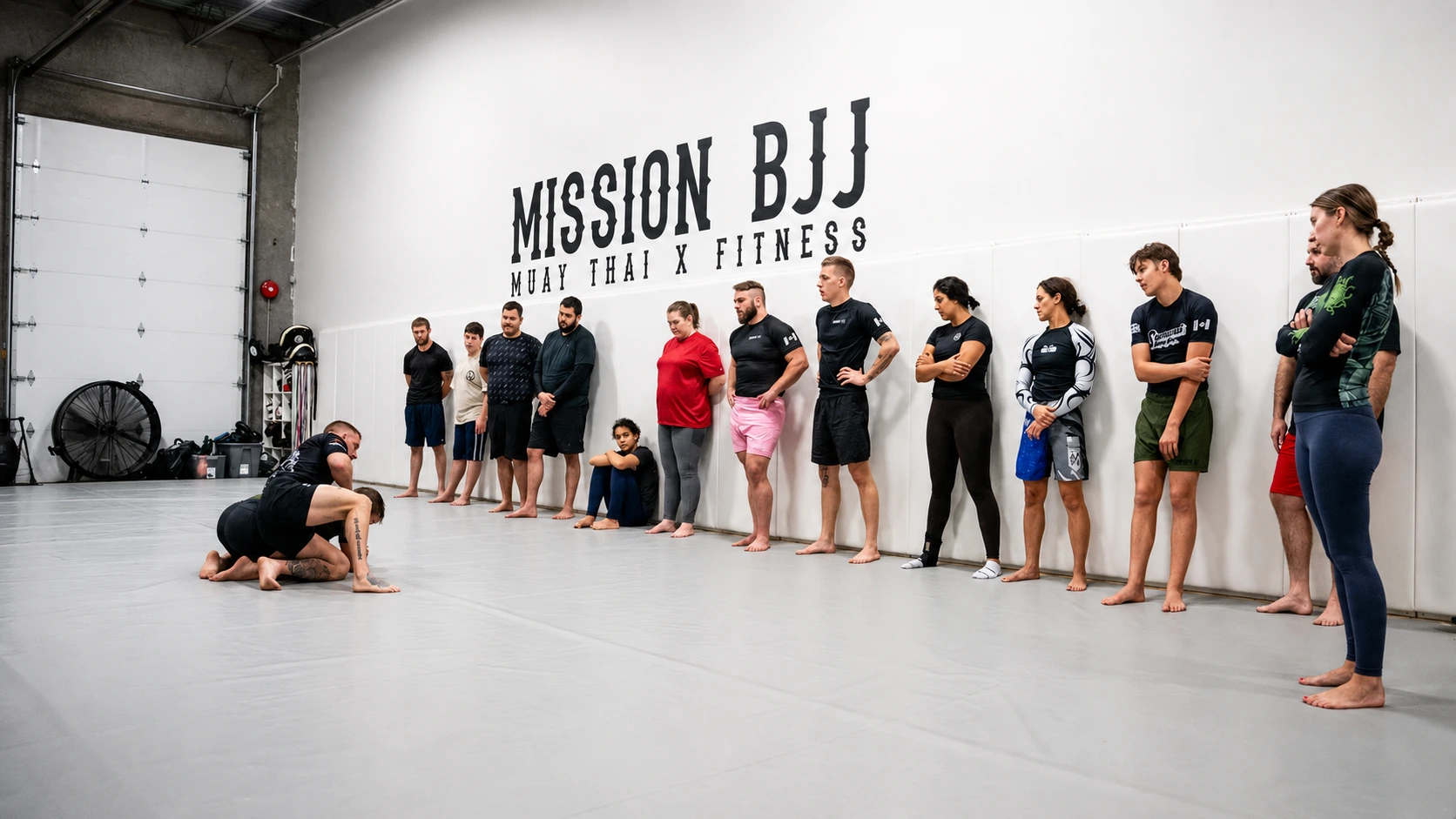 Members of all ages lined up on the mats in front of the painted Mission BJJ wall at the academy in Mission, BC